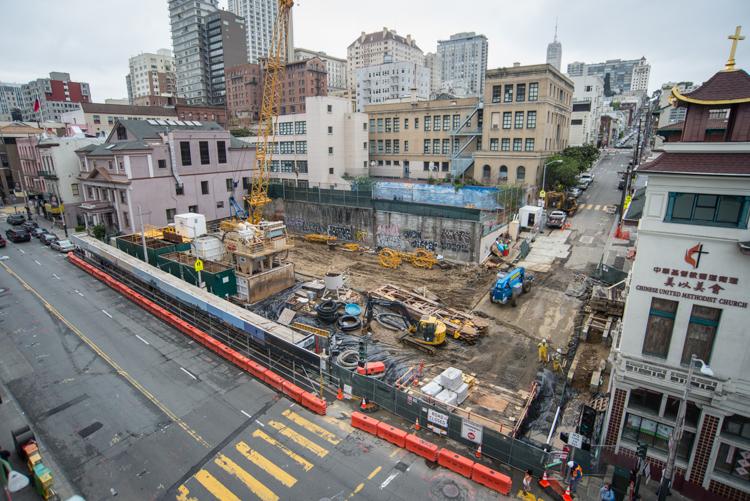 Chinatown Station construction site with excavation equipment, fencing, and surrounding historic buildings in San Francisco.