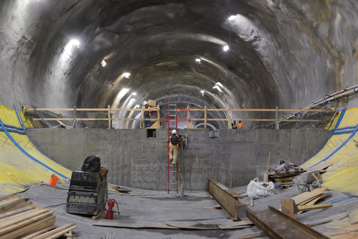 Construction workers in tunnel with yellow safety barriers and red ladder during Chinatown Station headhouse work.