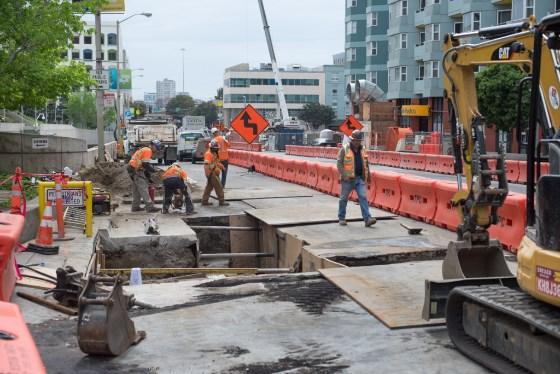 Construction crew working on water line upgrade at 4th Street with heavy equipment and traffic barriers in place.