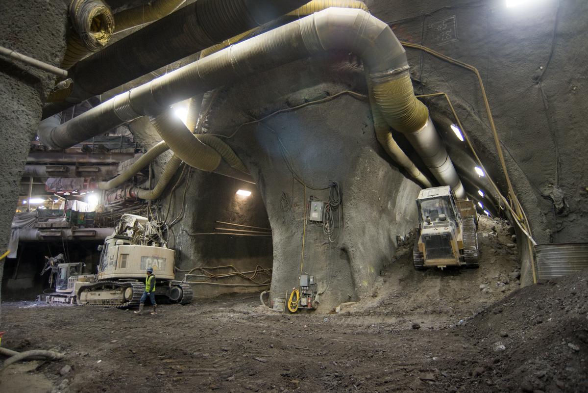 Underground tunnel construction with large concrete structure, metal piping, and heavy equipment including CAT machinery.
