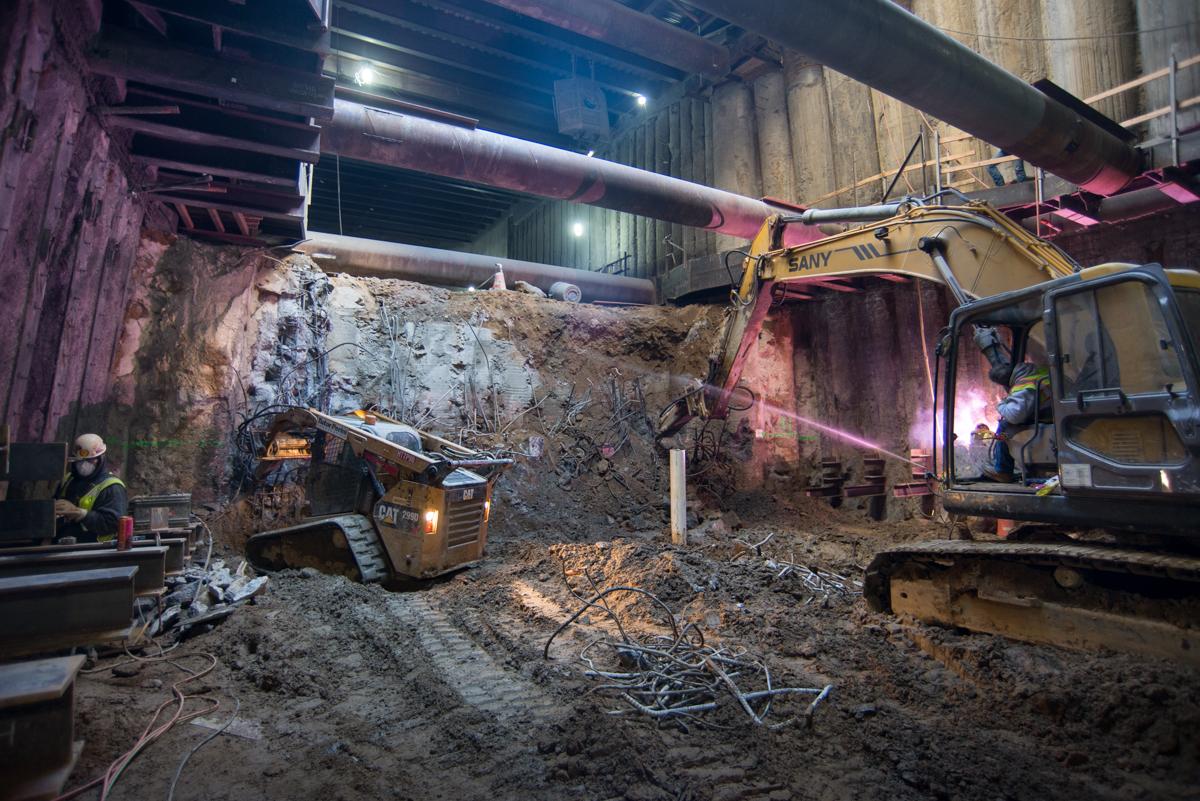 Construction crew operates excavation equipment inside underground station box to remove concrete.