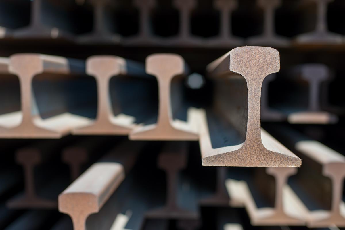 Close-up of stacked steel I-beam rails in storage yard near tunnel portal.