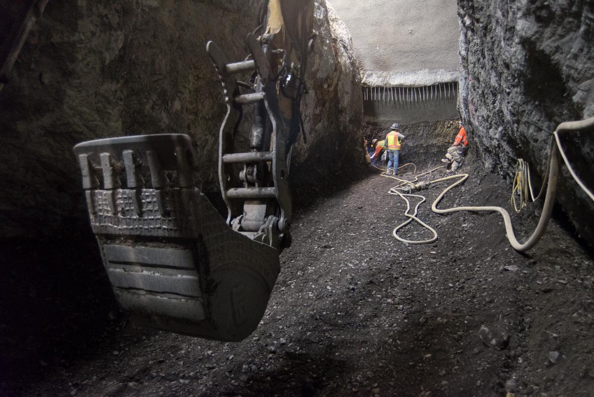 Bulldozer sorts excavated material in underground transit station construction site with workers nearby.