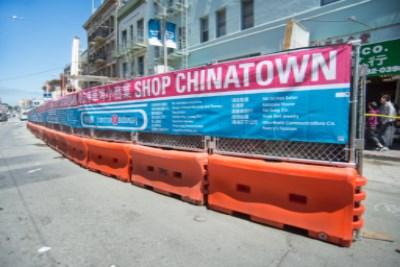 Cable car with Shop Chinatown banner on construction fence in San Francisco street.