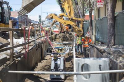 Yellow excavator positioned over trench during nighttime tunnel construction on urban street.
