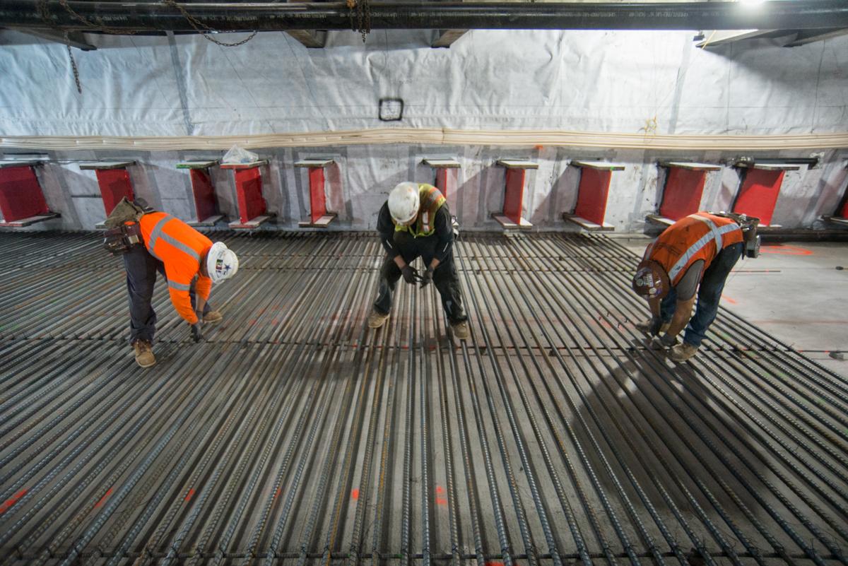 Three workers in safety vests inspect corrugated metal decking on a transit station floor.