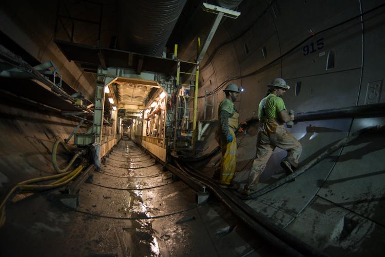 Workers in hard hats install conduit in an underground tunnel beneath 4th Street.