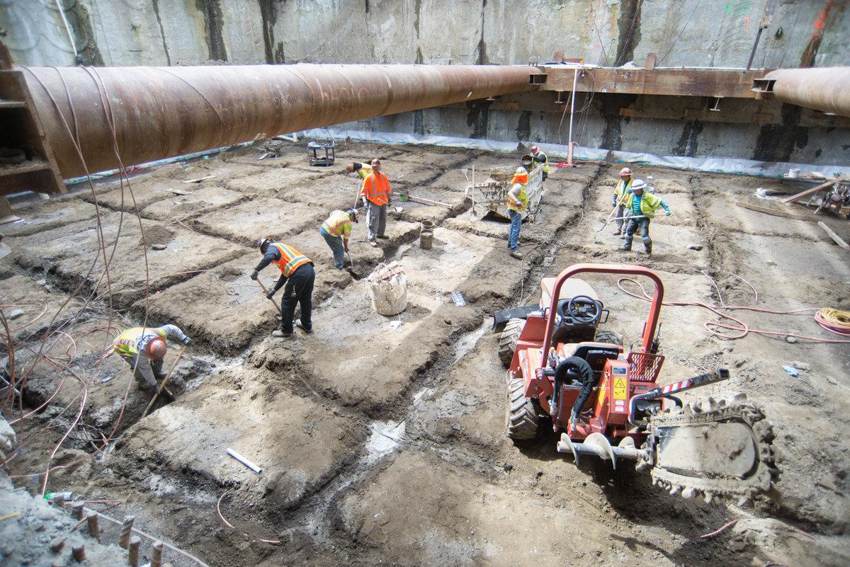 Workers in safety gear excavate and prepare foundation for concrete pouring at transit construction site.