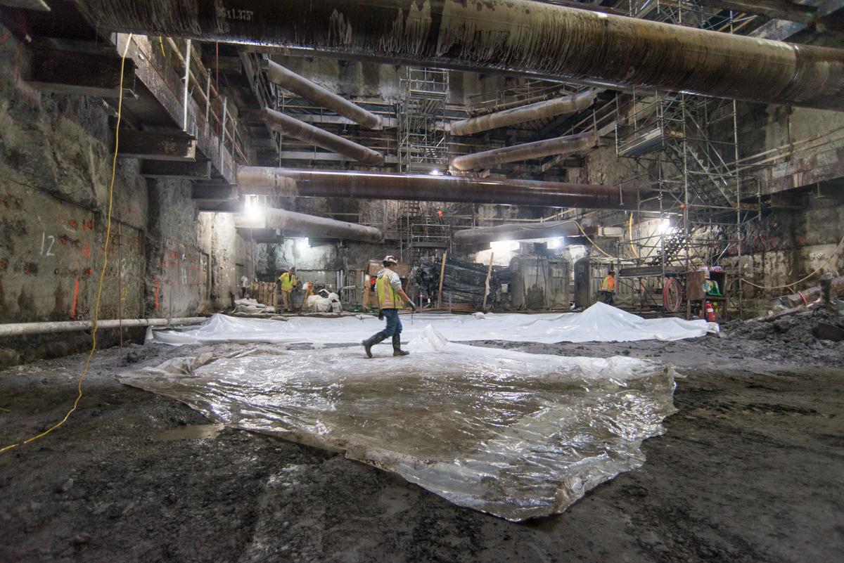 Workers lay plastic sheeting in underground station cavern during construction.