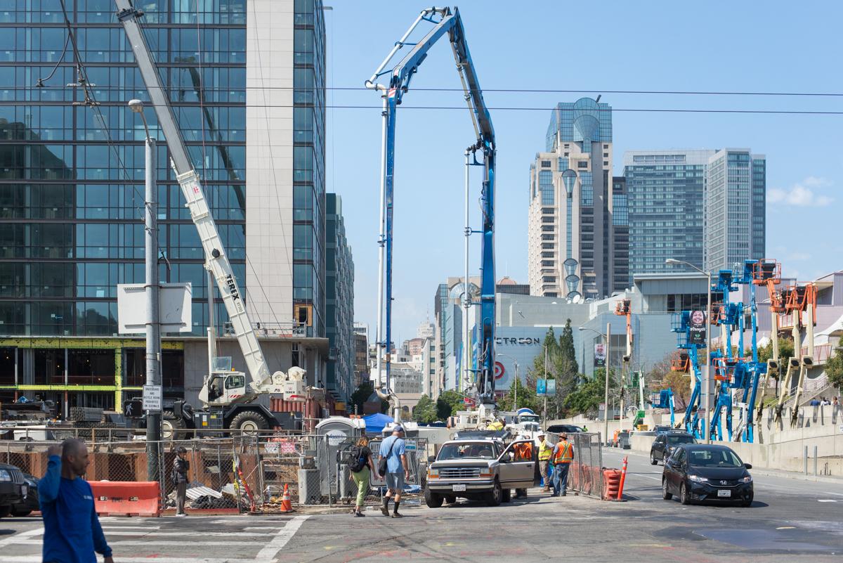 Construction equipment with concrete pump boom raised on 4th Street, downtown San Francisco, with traffic and pedestrians visible.