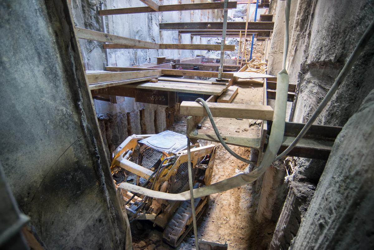 Compact excavator in narrow underground construction space with concrete walls and steel framing.