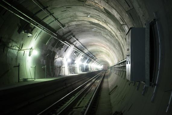 Northbound tunnel with railway tracks, fluorescent lighting, and concrete walls stretching into distance