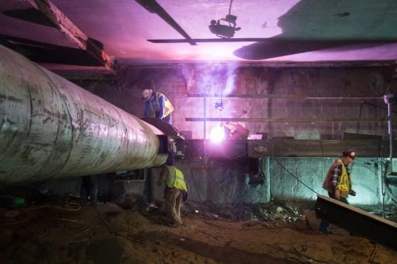 Workers welding steel supports inside an underground Central Subway station construction site.