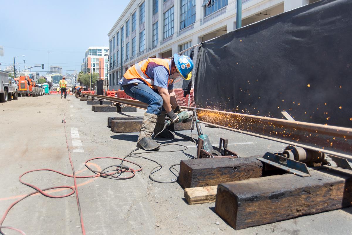 Worker in safety gear grinding a fresh rail weld on 4th Street for Central Subway construction.