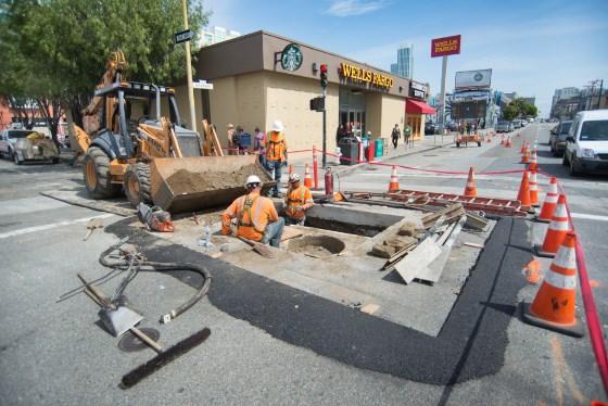 Construction workers upgrade utilities at street excavation site on 4th Street with heavy equipment and traffic cones.