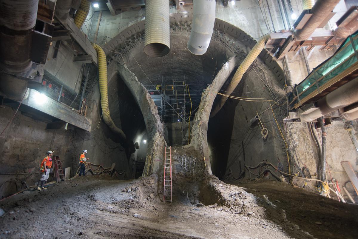 Underground tunnel excavation site with workers in safety gear and construction equipment at Chinatown Station.