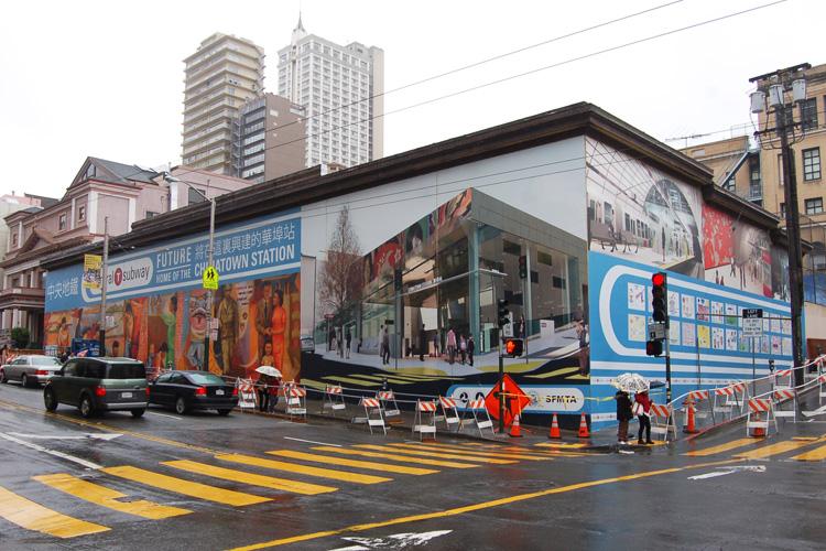 Chinatown Station construction site on Washington Street with temporary barriers and signage, surrounded by urban buildings and street infrastructure.