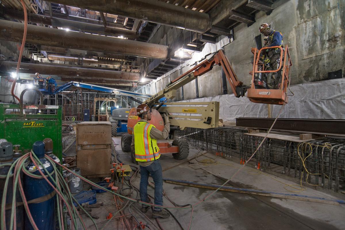 Workers operate a boom lift inside an industrial transit station under construction.