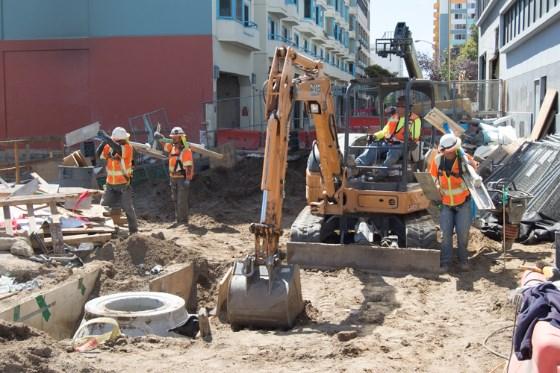 Construction crew operating excavator and equipment during underground utility installation work on urban street.