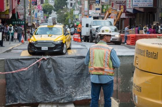 Construction worker at Stockton and Washington streets with traffic cones and yellow taxi nearby.