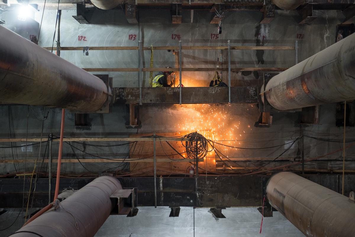 Worker welding structural bracing inside underground station construction site with sparks flying.