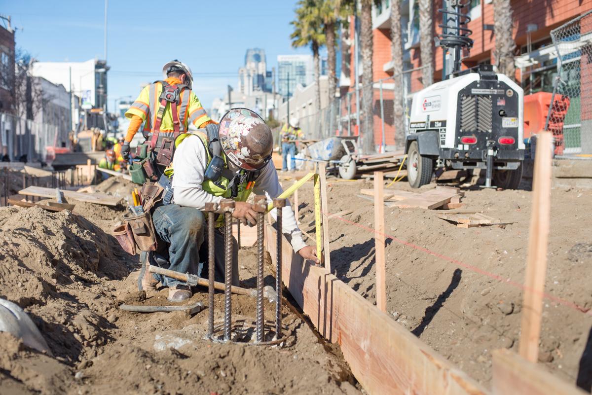 Construction workers install formwork for transit station foundation in urban excavation site.