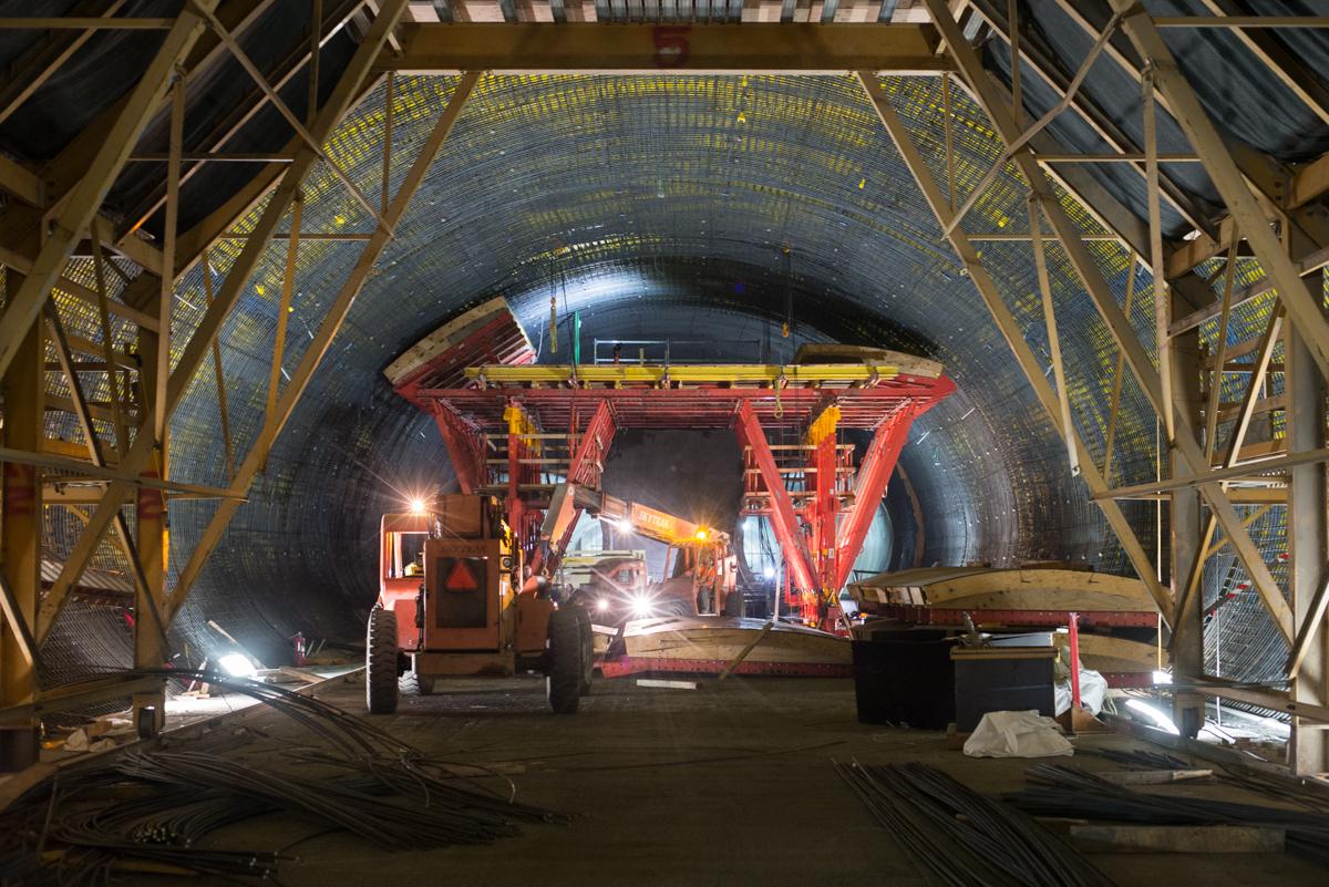 Red construction equipment and steel framework inside a curved concrete tunnel during transit station construction.