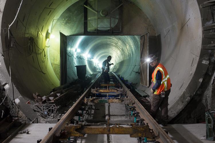 Workers install rail inside illuminated tunnel under 4th Street station box.