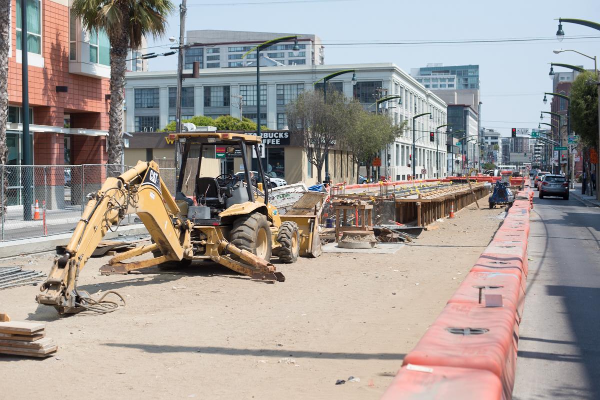 Construction equipment and wooden forms along urban street during transit station platform work.