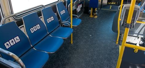 Interior of a transit bus showing blue priority seats with yellow handrails and dark flooring.