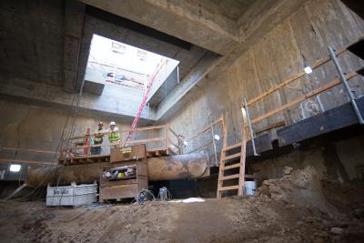 Construction site interior with drill rig, wooden scaffolding, and concrete roof structure under excavation.