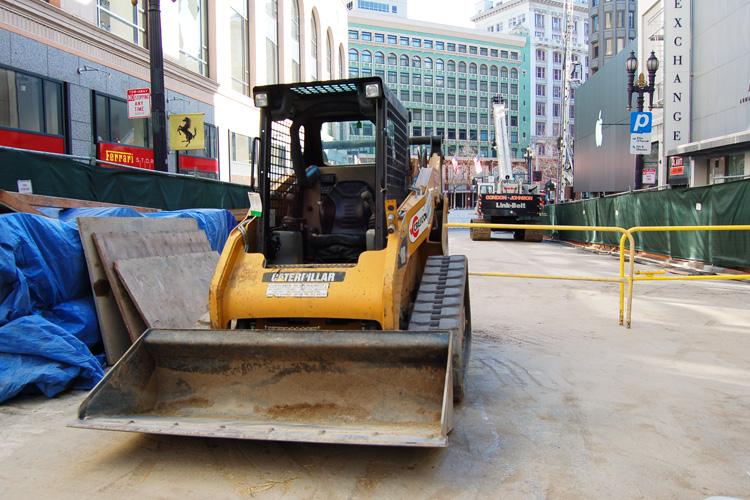 Yellow Caterpillar skid steer loader with bucket attachment on urban street construction site near Union Square.