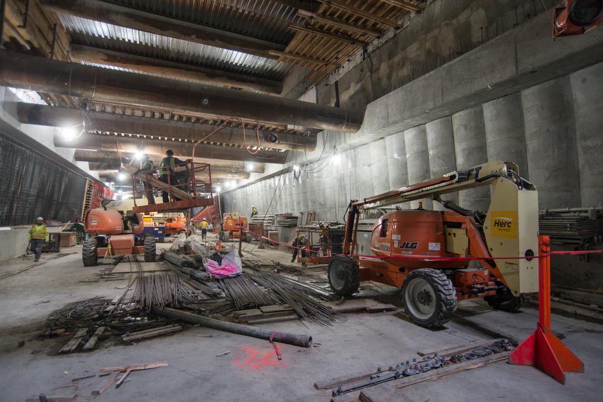 Construction workers operate heavy equipment inside an underground transit station during platform construction.