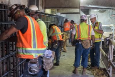 Construction workers in safety vests and hard hats gather in an underground tunnel during headhouse construction work.
