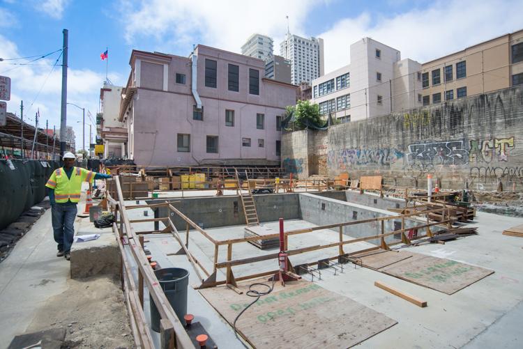 Construction site with excavation pit, wooden framework, and worker in safety vest on Stockton Street.
