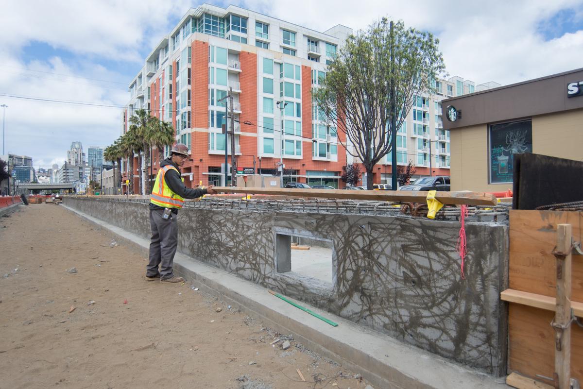 Construction worker in safety vest inspecting concrete platform foundation walls at 4th and Brannan surface site.