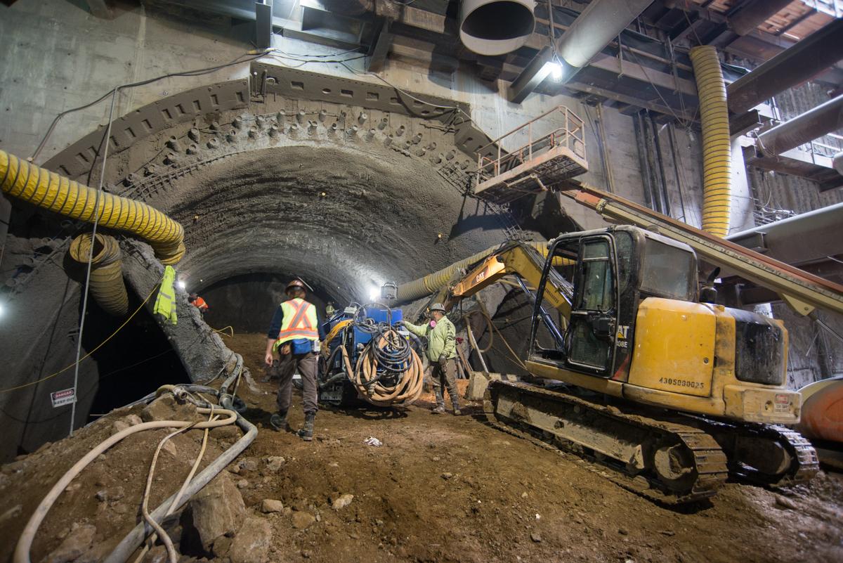 Workers operate shotcrete equipment inside an underground tunnel excavation for the Central Subway project.
