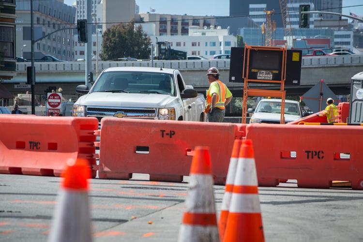 Construction work on 4th Street with red barriers, traffic cones, and workers in safety vests near a white pickup truck.