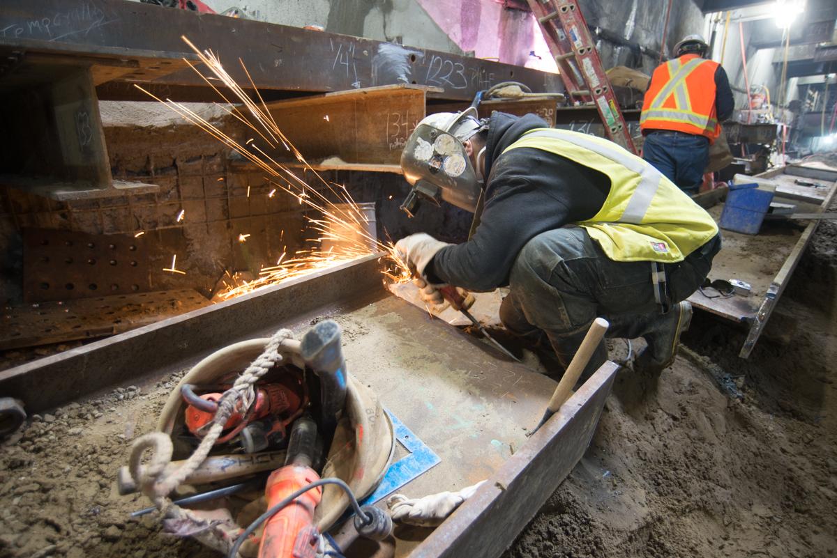 Worker grinding steel beam for temporary bracing on 4th Street construction project.