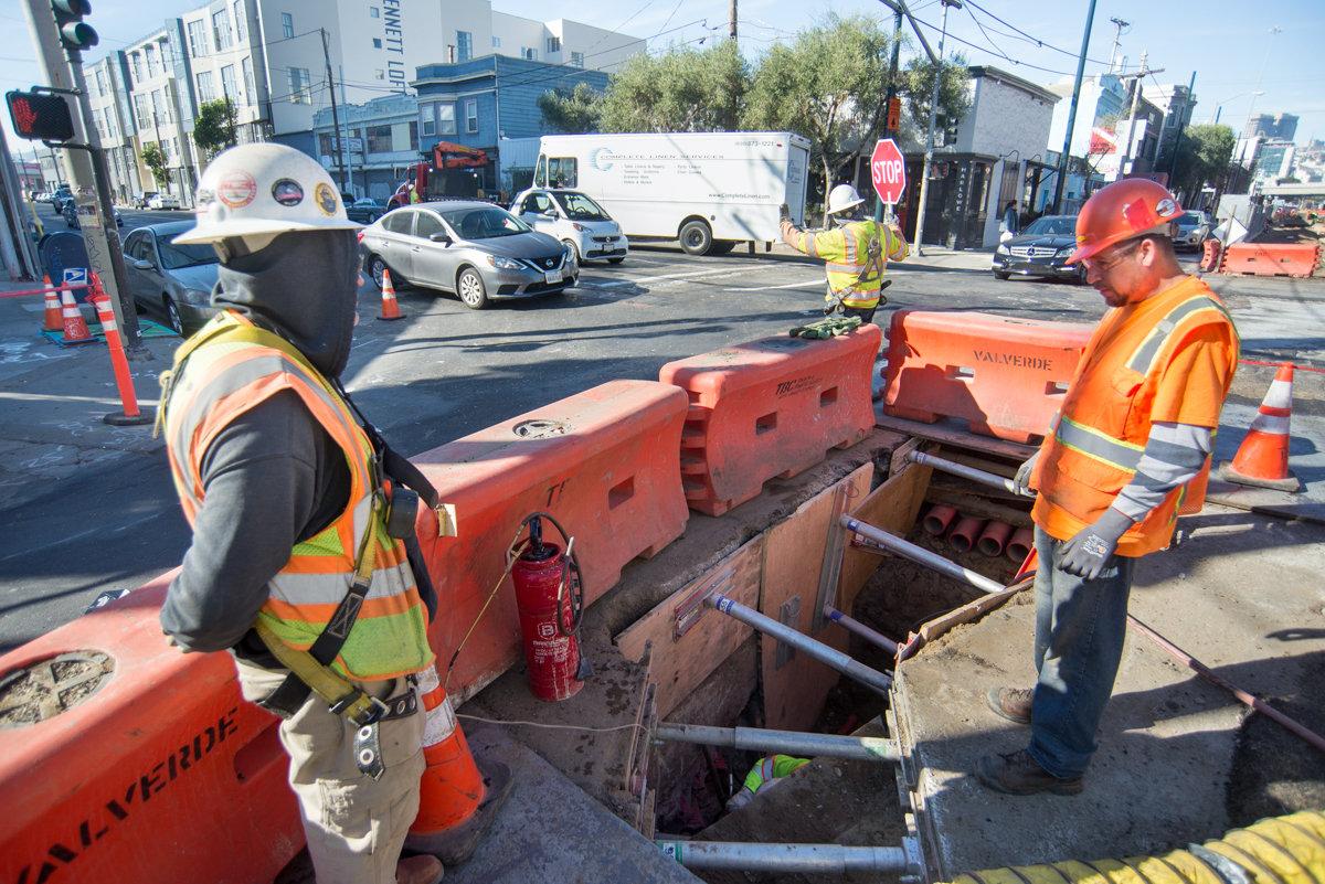 Construction workers in safety gear installing utility ducts at 4th and Brannan station foundation work site.
