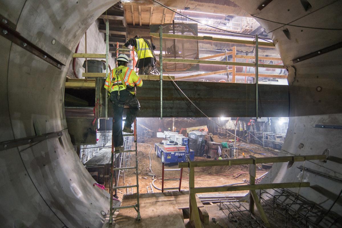 Worker in safety gear descending ladder into underground transit tunnel construction site.