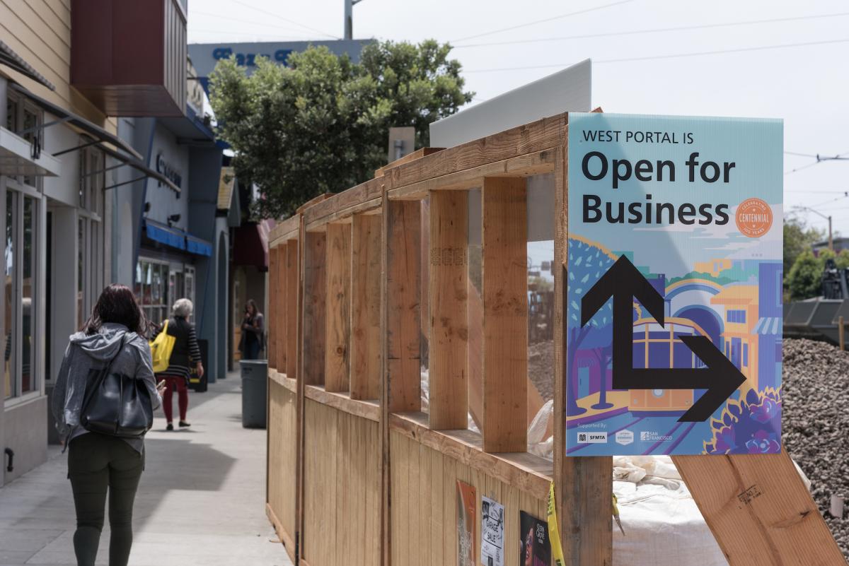 West Portal Avenue pedestrian area with wooden barriers and Open for Business signage promoting local merchants.
