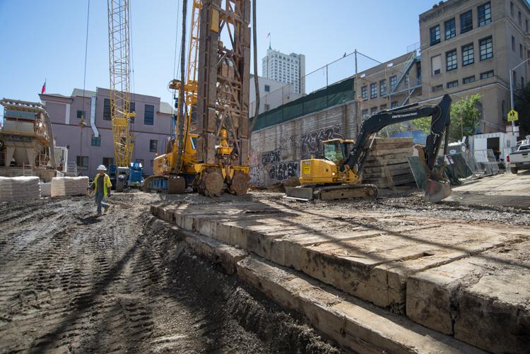 Construction site with excavation equipment and workers preparing underground foundation work in urban area.