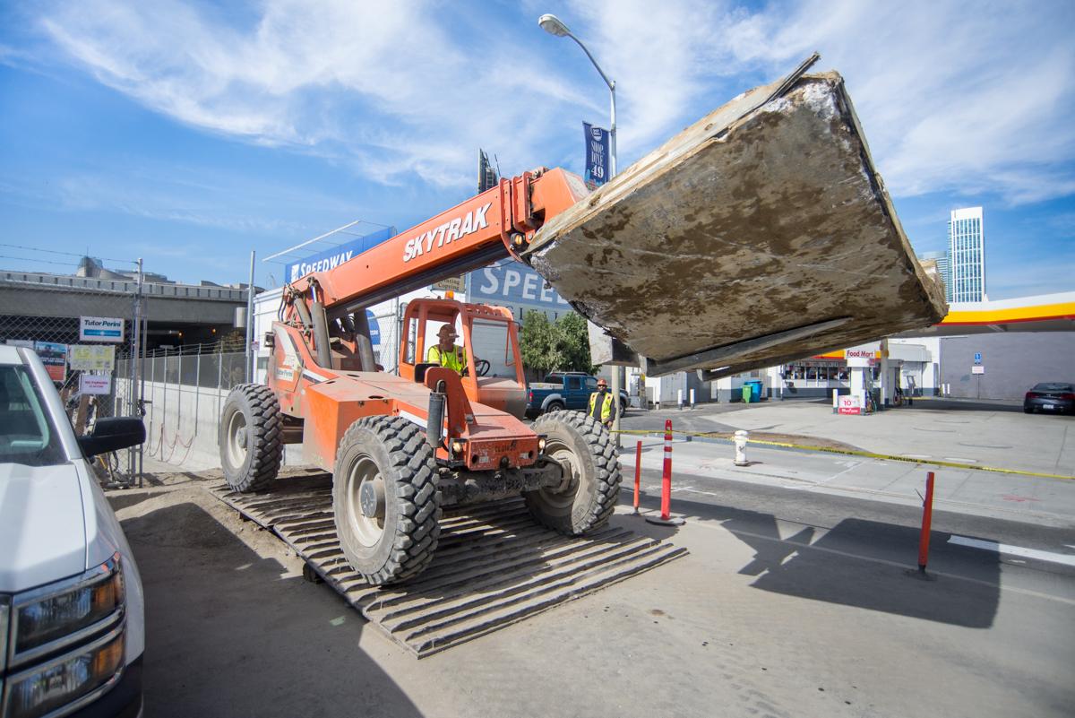 Orange telehandler lifting concrete tunnel section at transit station construction site.