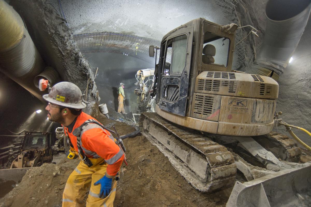 Workers in safety gear operate excavation equipment inside an underground tunnel during Central Subway construction in Chinatown.