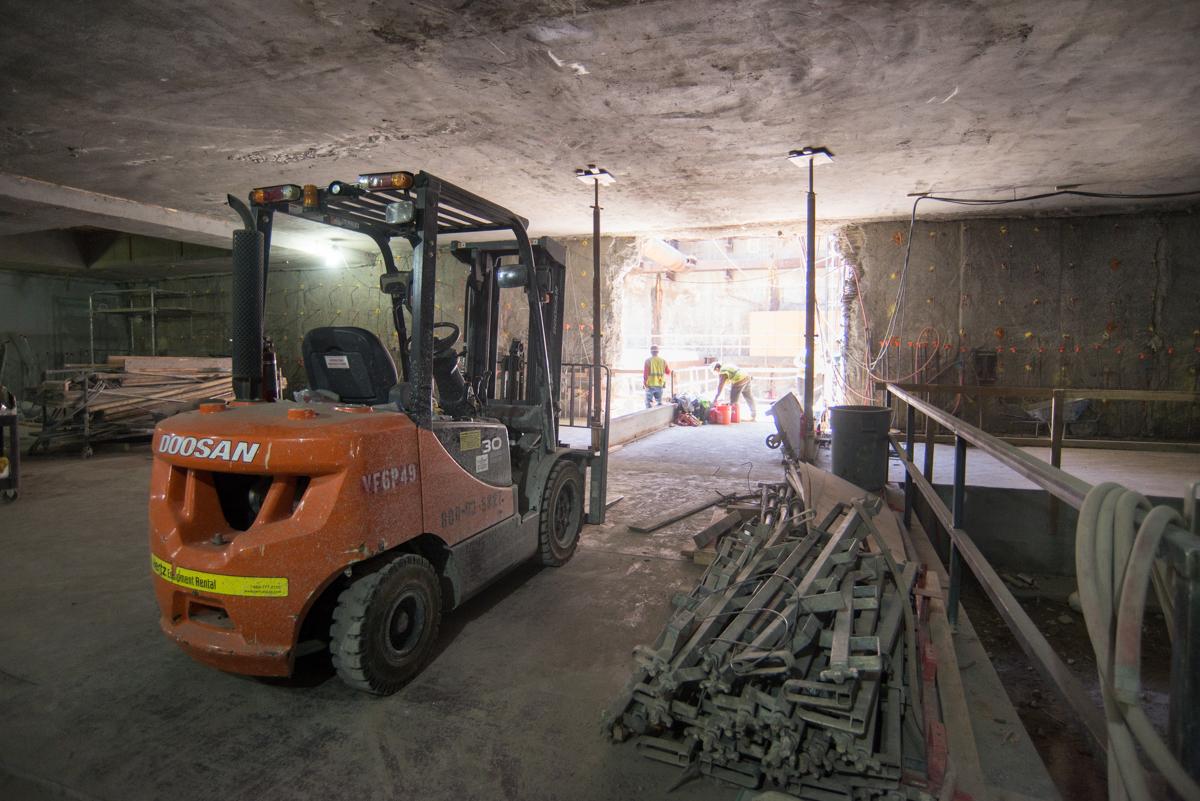 Forklift moving materials inside underground station construction site with workers and equipment visible in background.