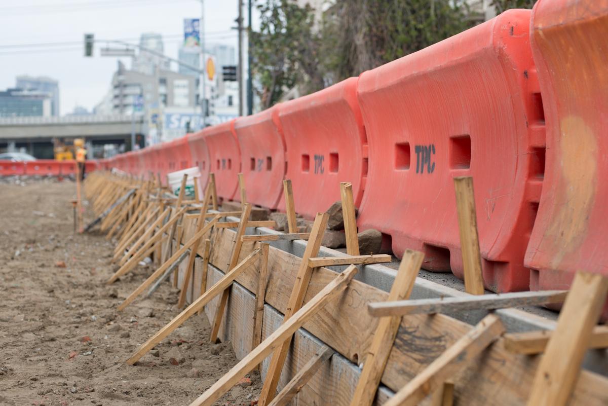 Red barrier sections with wooden forms along construction site near urban street.