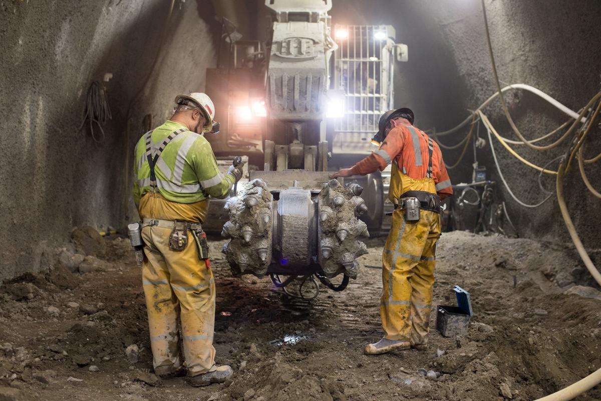Two workers in safety gear inspect equipment in an underground tunnel lit by work lights.