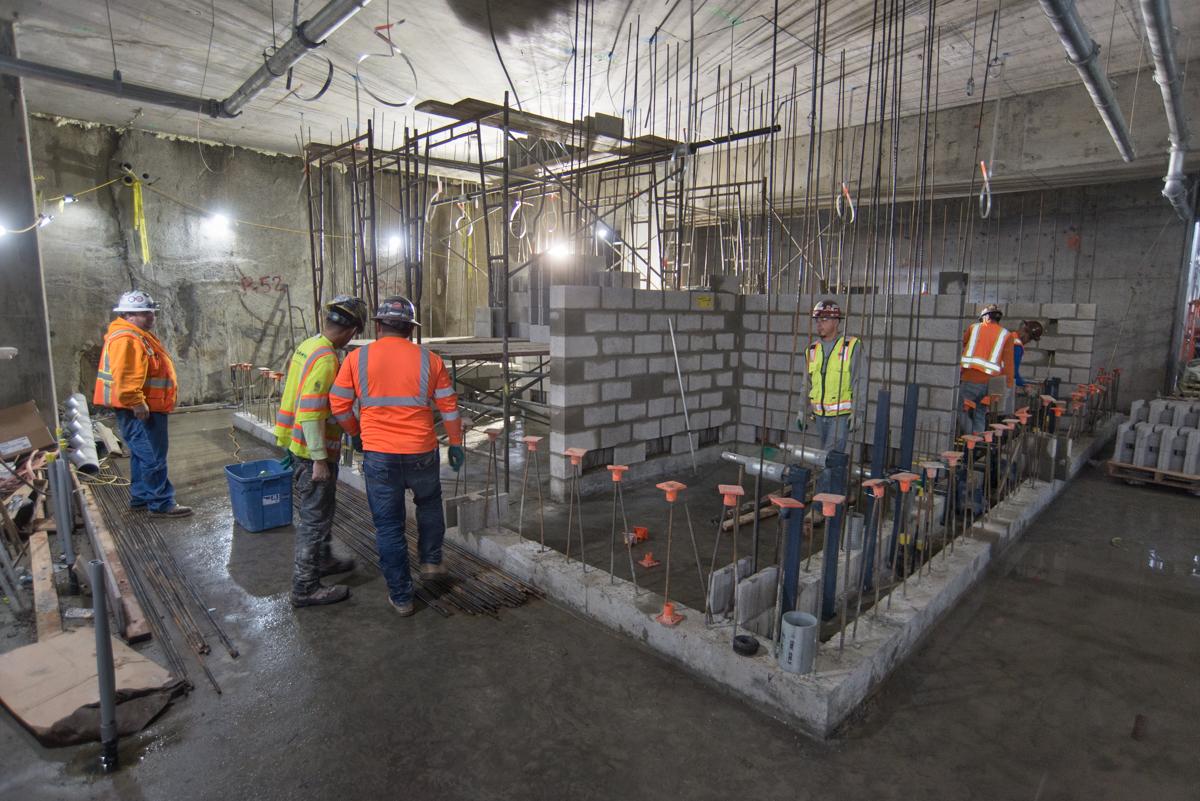 Construction workers in safety gear assemble concrete forms and rebar cages in an underground transit station concourse.