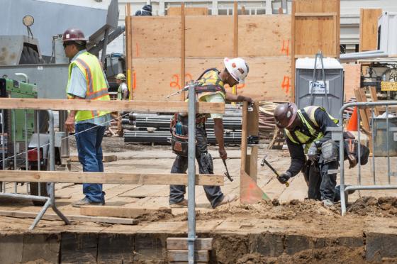 Construction workers assemble wooden safety fencing at a Central Subway station construction site.